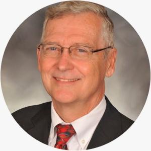 White male with glasses, black jacket, white shirt, and a red patterned tie